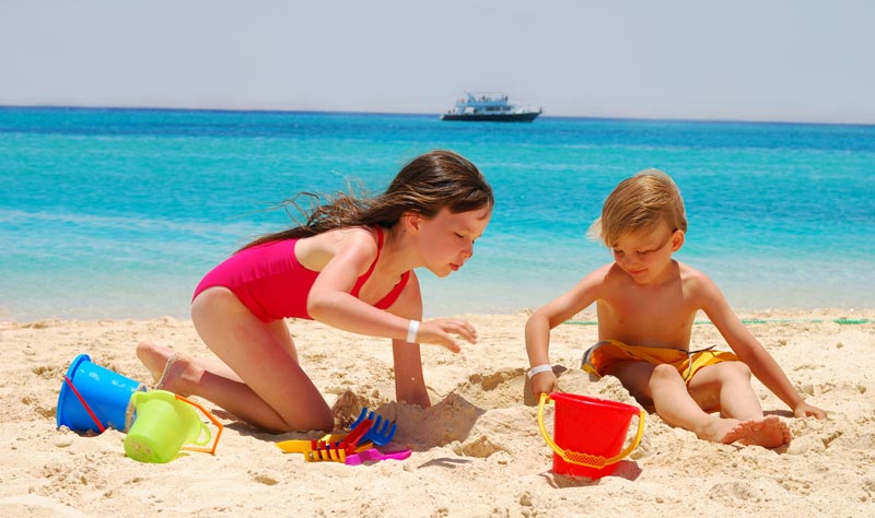 brother and sister playing in the sand at the beach