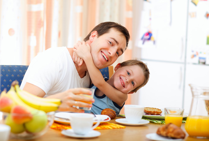 child loving his father while eating breakfast