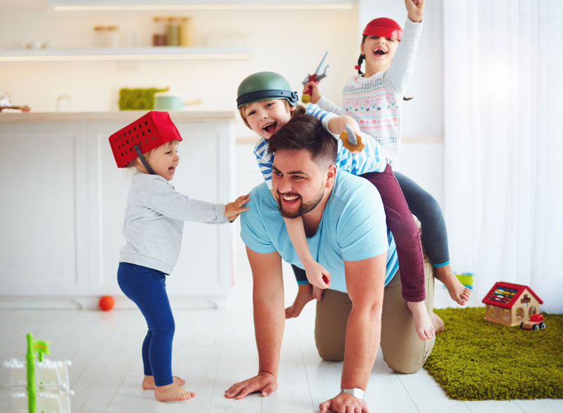 crew of young kids riding on dads back while he is crawling on the floor