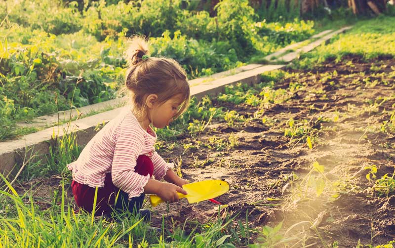 cute little girl playing outside in the dirt and grass with a shovel
