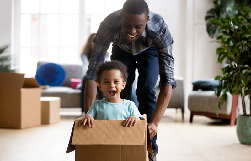 dad pushing young boy in cardboard box across the floor