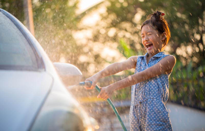 elementary age girl washing a car by spraying water from a hose