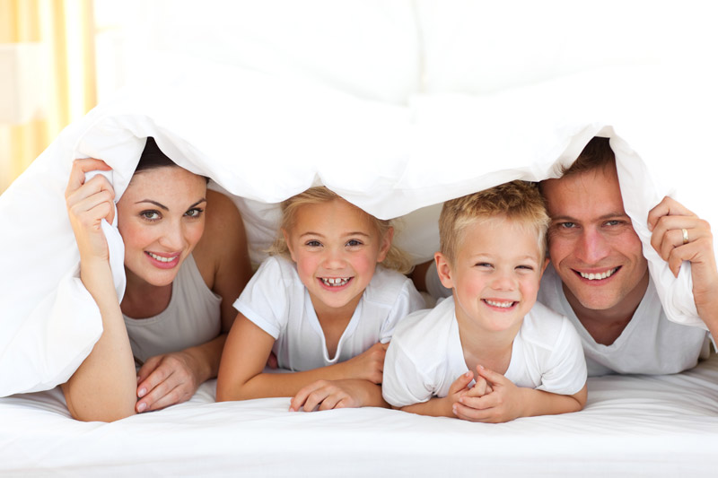 family with two young children hiding under a blanket