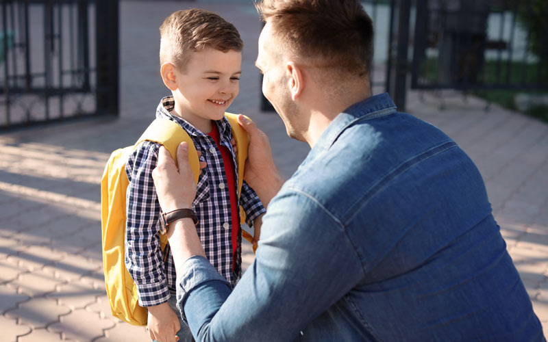 father adjusting school backpack on smiling young sons back