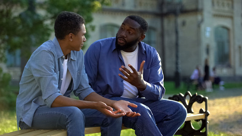 father and son chatting together while sitting on a park bench