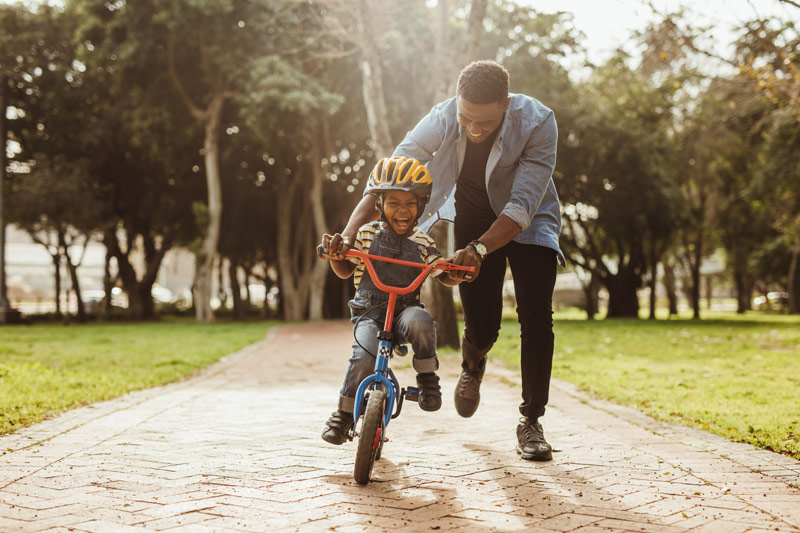father helping child to learn to ride bike