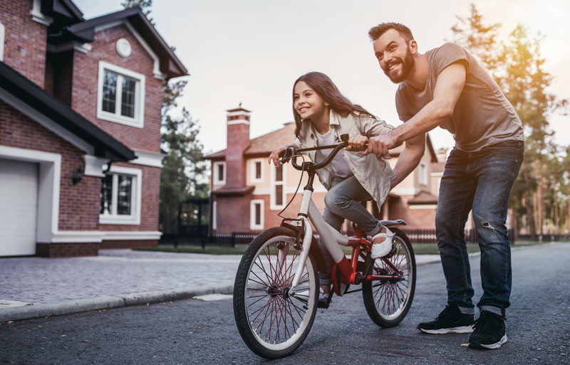 father helping daughter learn how to ride a bike