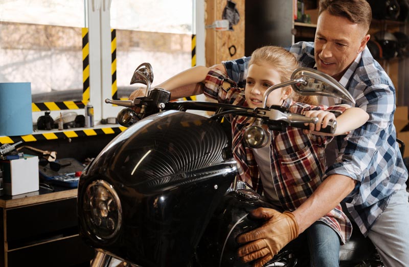 father helping young daughter sit on a motorcycle