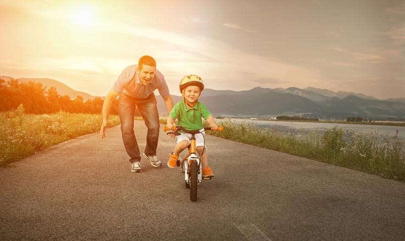 father helping young son learn how to ride a bike