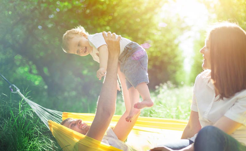 father in hammock holding up younger child