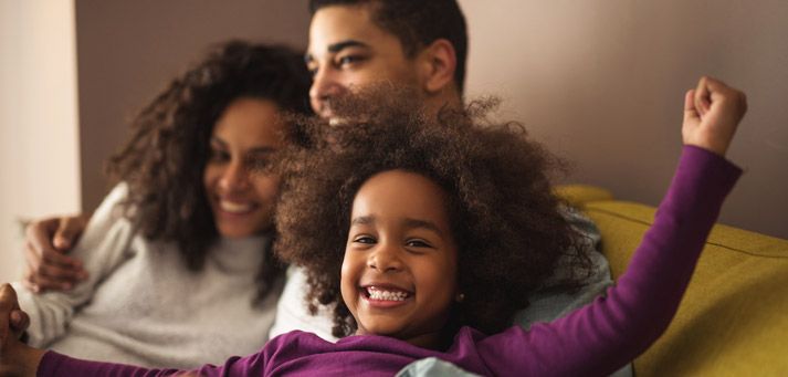father snuggling with wife and child on the sofa