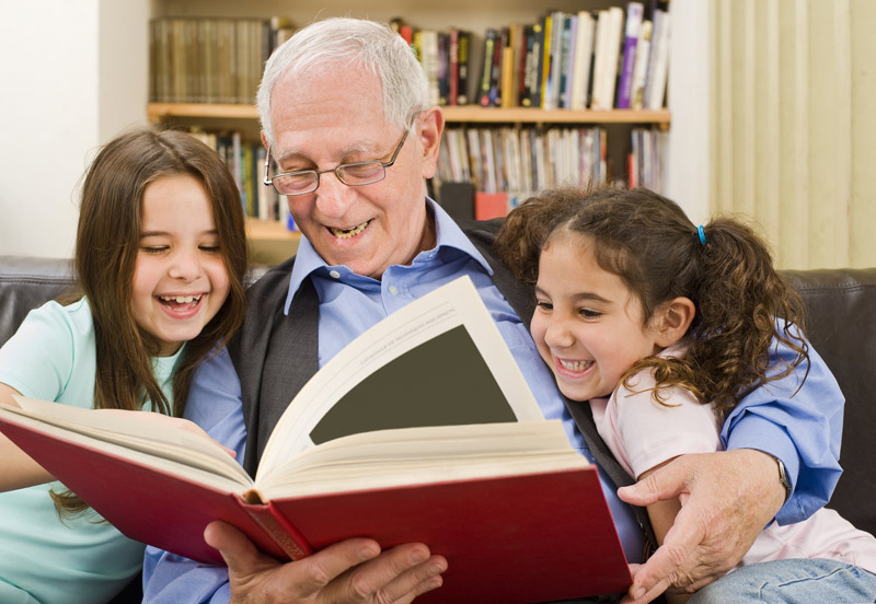 grandfather reading a book to two young girls