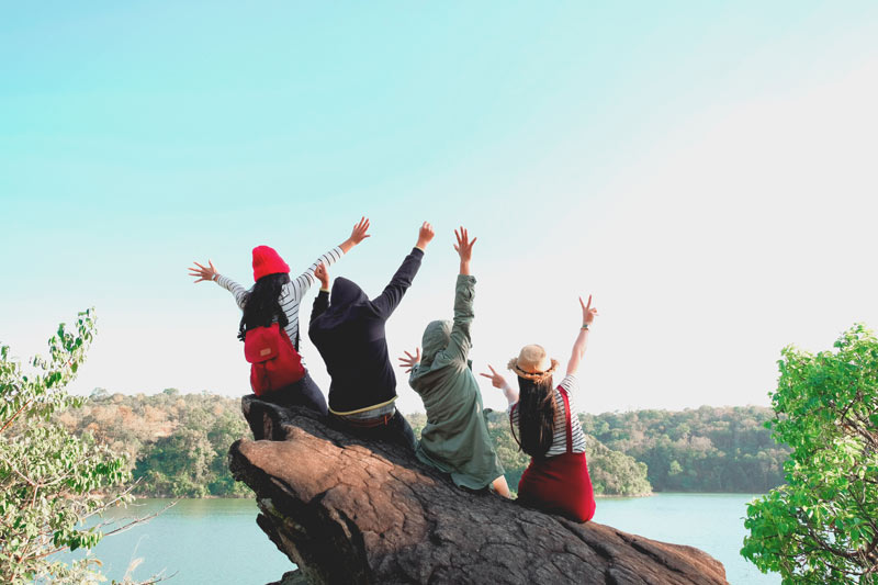 group of friends sitting excitedly on a rock over the water