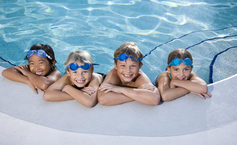 group of kids smiling and leaning against edge of pool