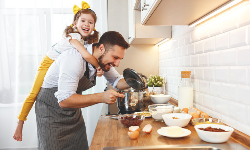 happy little girl hanging on chef dads back in the kitchen