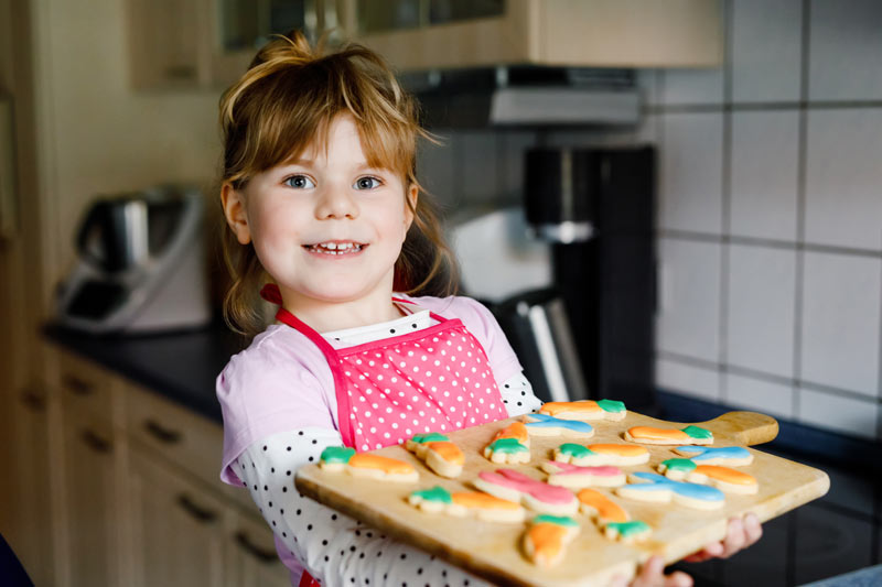 happy little girl in kitchen holding fresh baked cookies