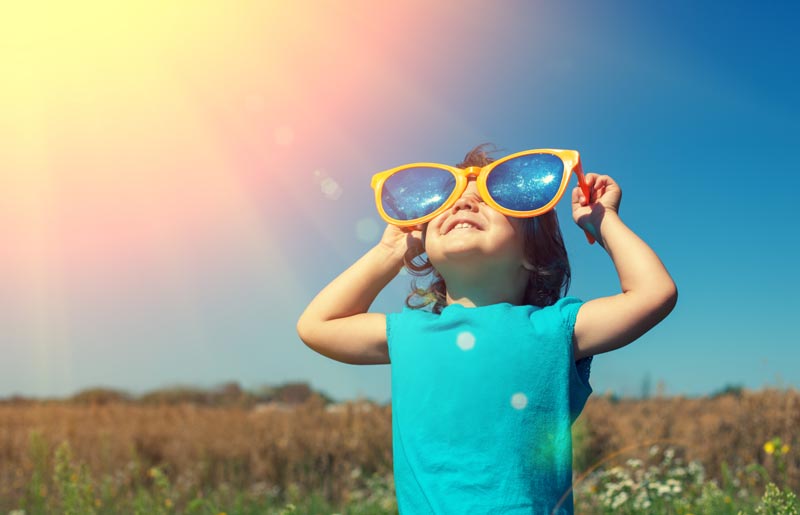 happy little girl standing in the sun wearing giant, oversized sunglasses
