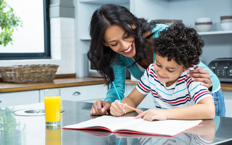 happy mom helping elementary aged son with homework and snack