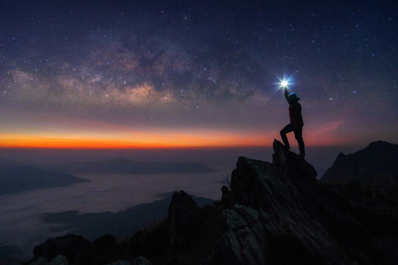 hiker standing on rock in dark and holding up a flashlight