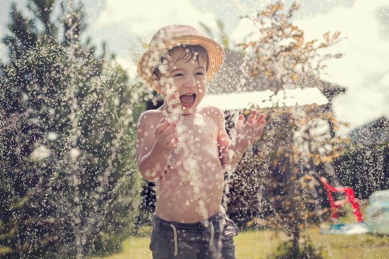little boy playing outside with water sprinklers