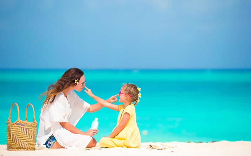 little girl and mother at the beach applying sunblock lotion onto each other