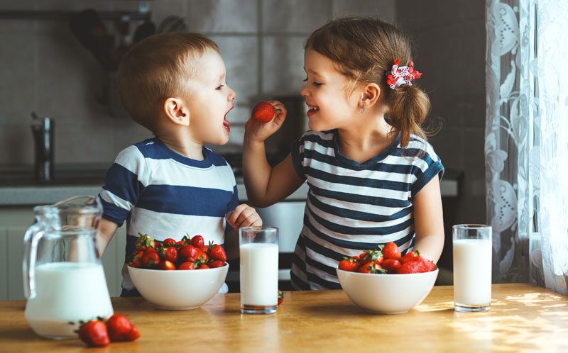 little girl feeding younger brother strawberries and milk