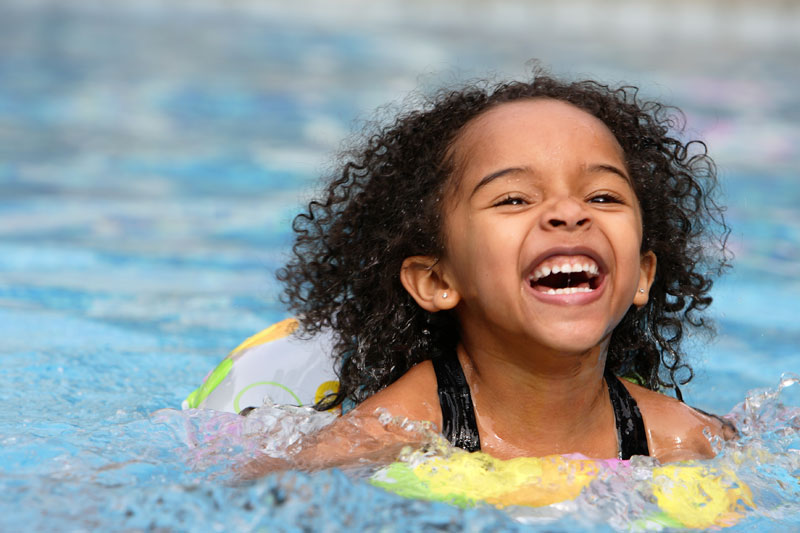 little girl laughing as she swims on float in water