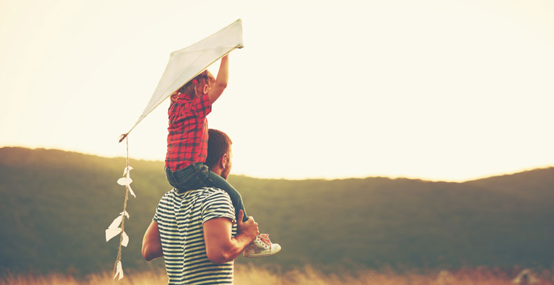 little girl sitting on dads shoulders while holding a kite