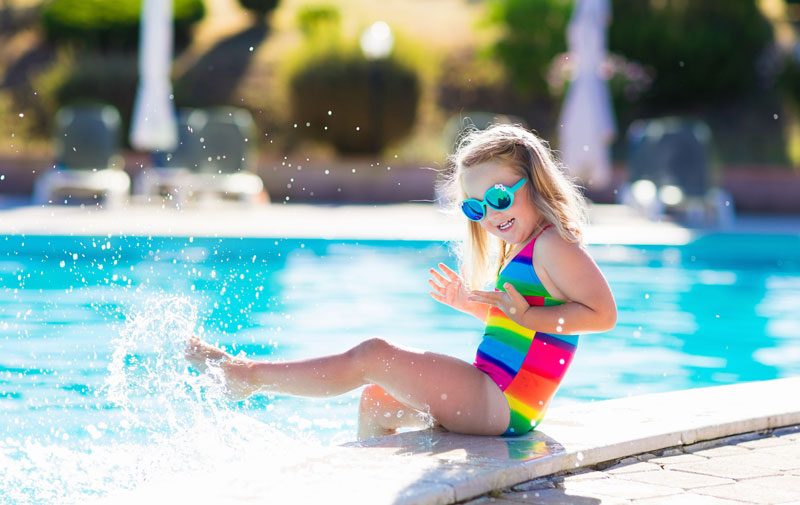 little girls sitting on edge of pol kicking and splashing water