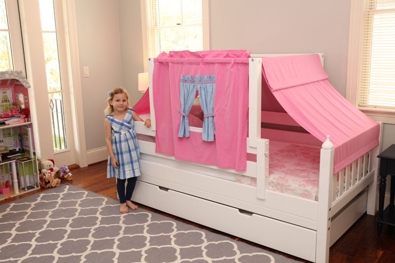 little girl standing by Maxtrix decorated toddler bed with pink curtain
