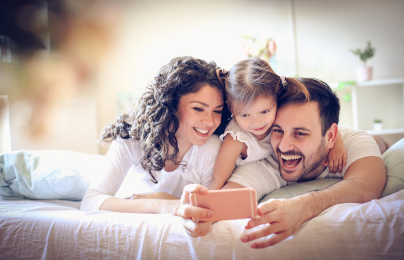 mom and dad and young daughter taking a selfie on the bed