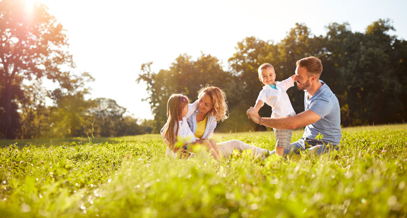 mother and father happily sitting on the grass with their two young children