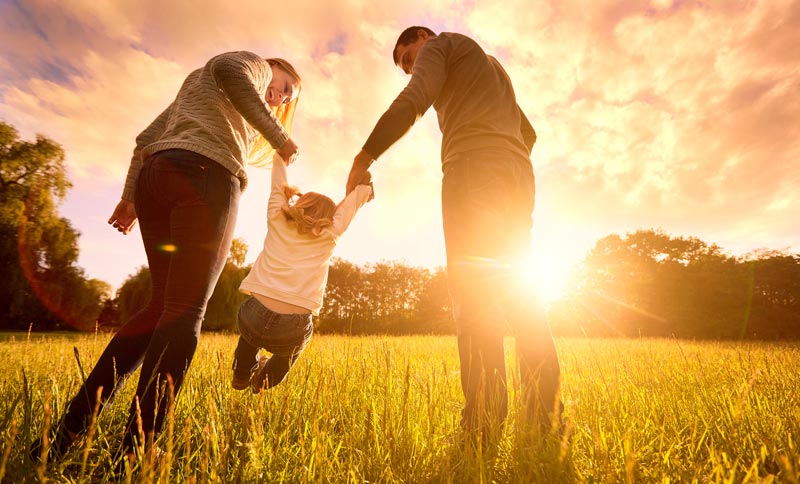 mom and dad swinging young child over tall grass