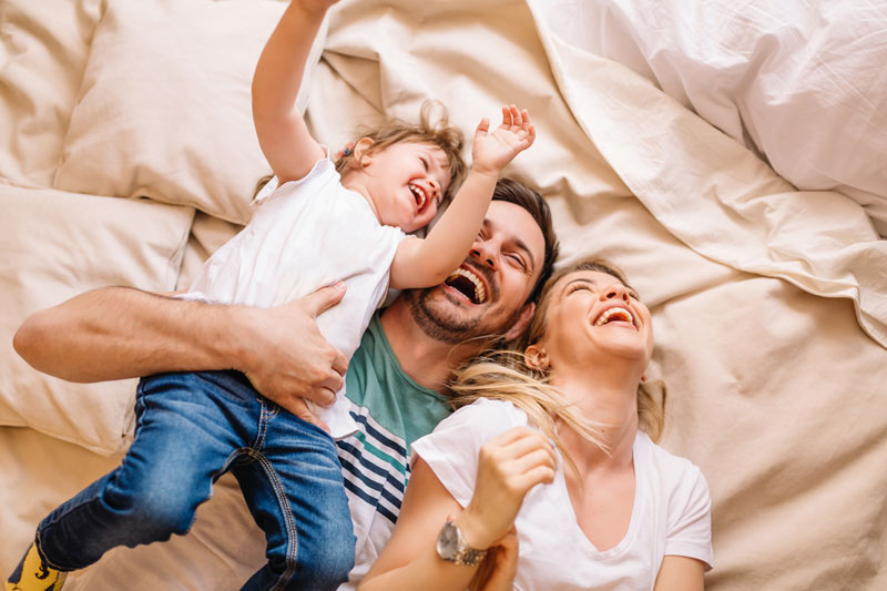 mom dad and toddler on bed laughing