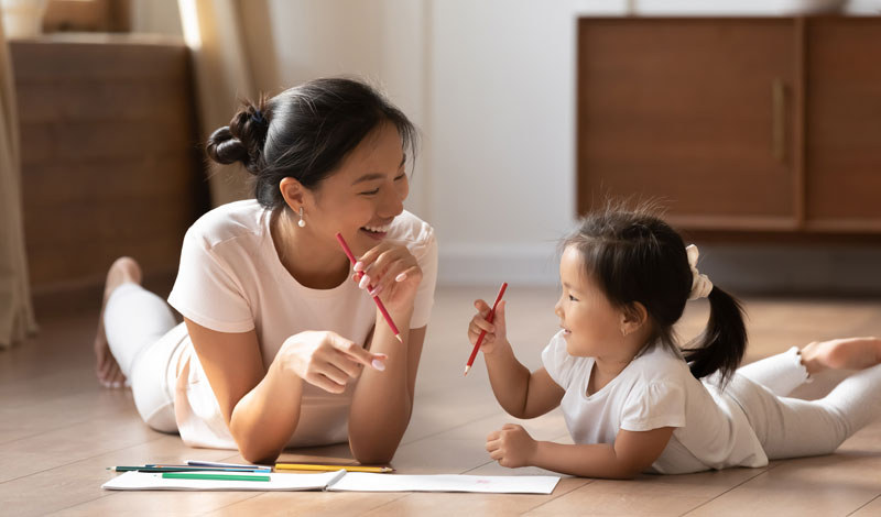 mom helping young girl on floor learn how to hold her pencil