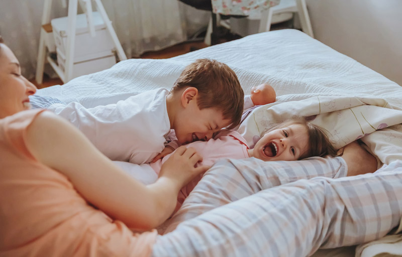 mom playing with young kids on bed mattress