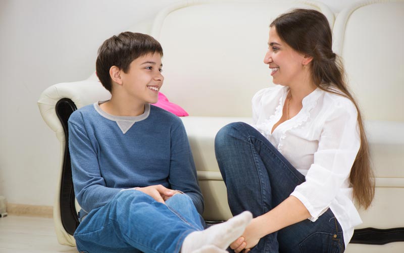 mother and son chatting while sitting on the floor in front of a sofa