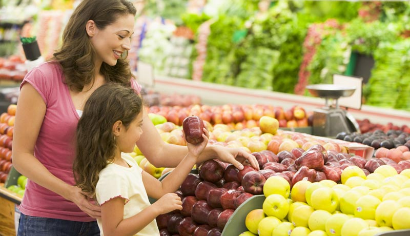 mother and young daughter examining apples in a grocery store