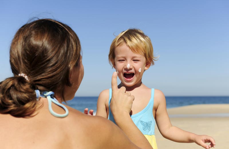mother applying sunblock lotion on child at beach