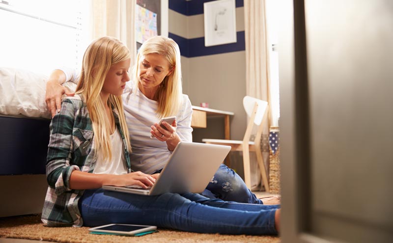 mother helping daughter with her homework while sitting on the floor with laptop