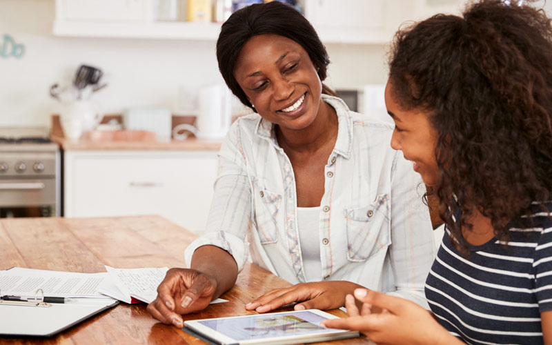 mother helping teen daughter with homework while in kitchen