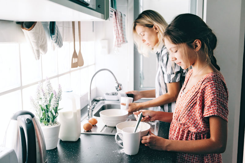 mother in the kitchen baking with her preteen daughter