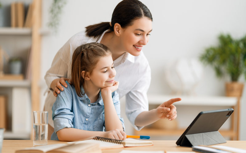 mother pointing out items in young daughters homework on tablet