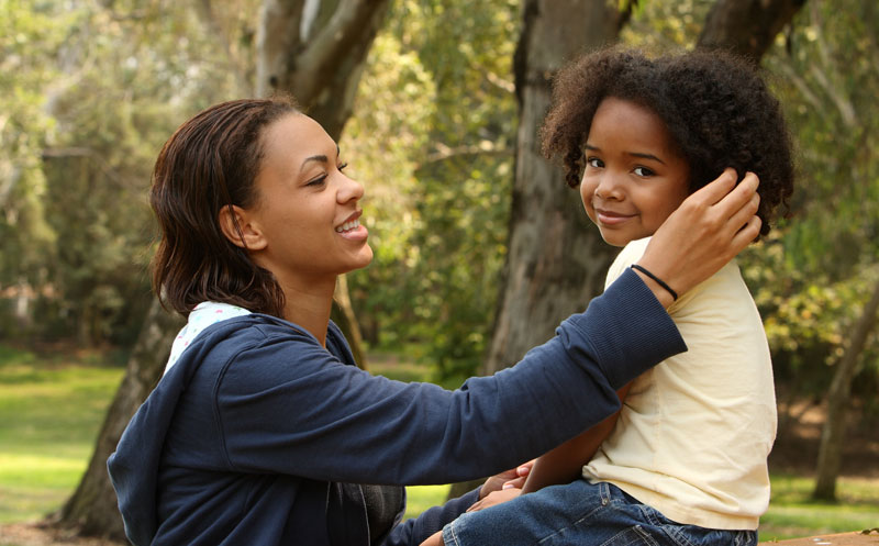 mother talking to young daughter who is sitting on a picnic table