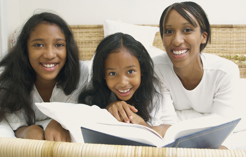 mother with two daughters reading a book while lying in bed