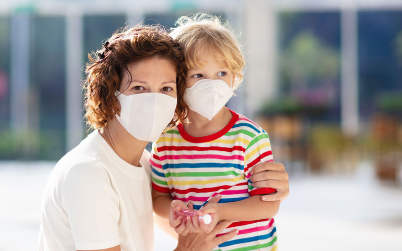 parent and young child wearing facemasks and holding hands with sanitizer