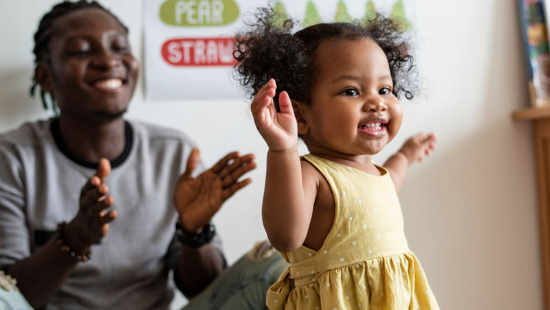 parent encouraging young girl who is learning how to walk