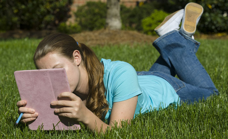 preteen girl in the grass journaling about her day