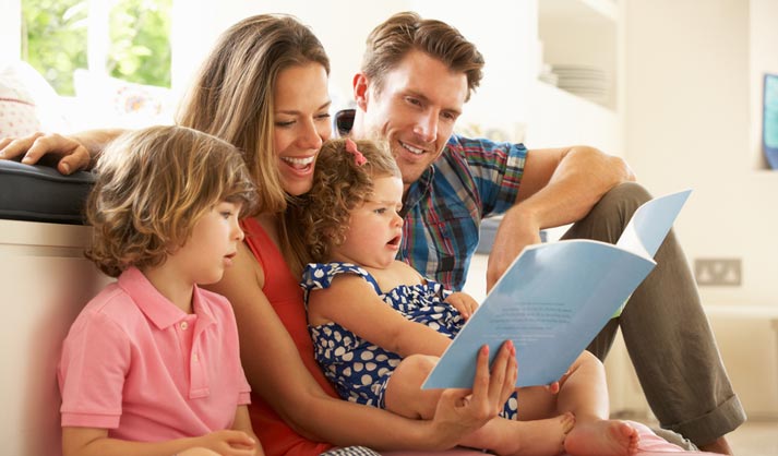family sitting on a sofa reading together out loud a kids book