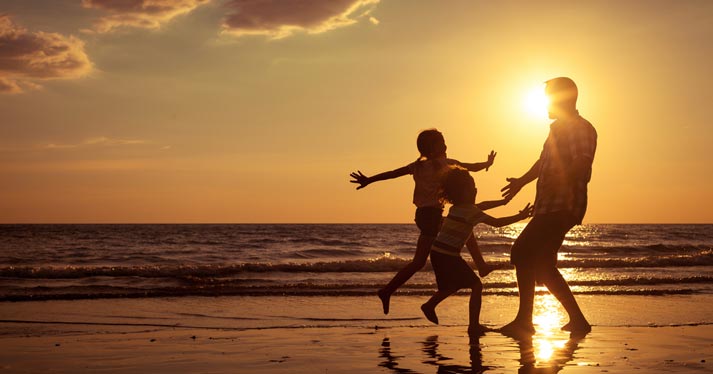 kids and father running by the waves as they lap on a beach